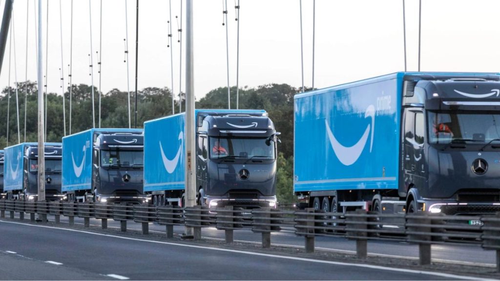 A convoy of Amazon-branded electric trucks driving over a bridge in the UK